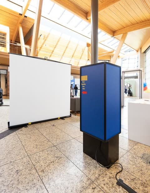 Aviation-themed Pick-A-Booth kiosk with a boarding-pass wrap and white backdrop in a bright Calgary hall.